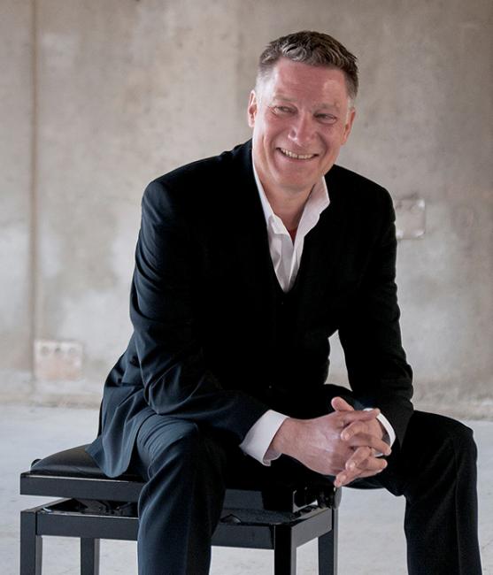 Mårten Landström sitter på en pianopall framför en solbelyst betongvägg